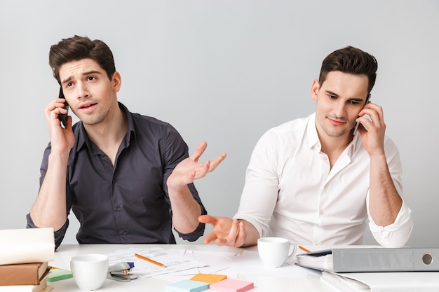 Handsome two young business men talking by mobile phones.