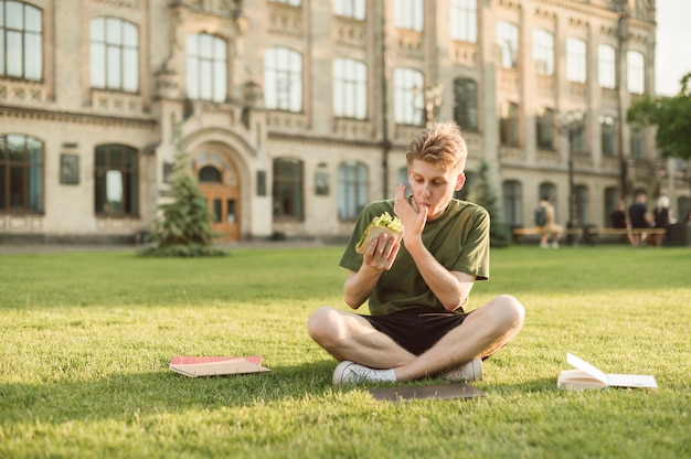 Handsome university student eating appetizing sandwich