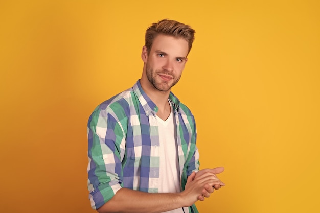 Handsome unshaven guy portrait keep hands together in checked shirt yellow background serious