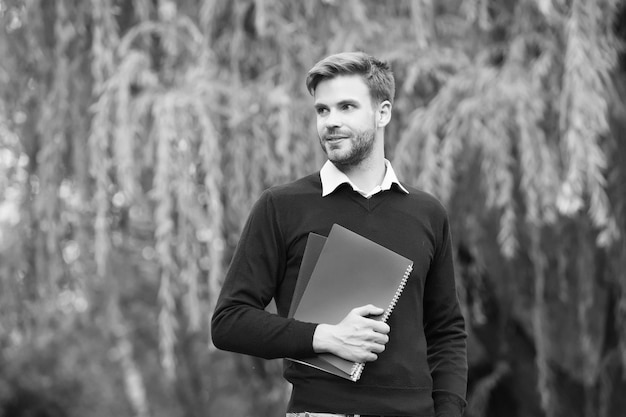 Bell'uomo con la barba lunga con una cartella di lavoro nelle sue mani che fissa la giornata della conoscenza all'aperto in lontananza