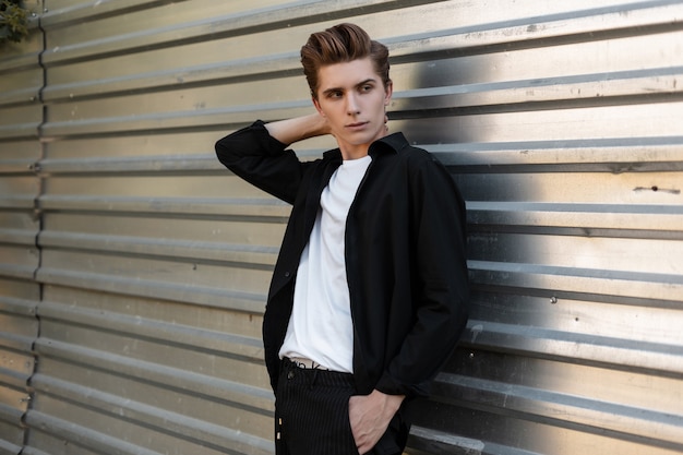 Handsome urban young man with a fashionable hairstyle in an elegant black shirt  near metal silver wall 