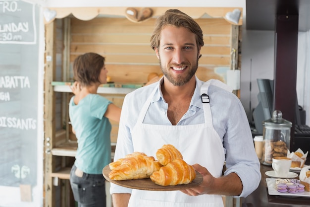 Handsome waiter holding tray of croissants