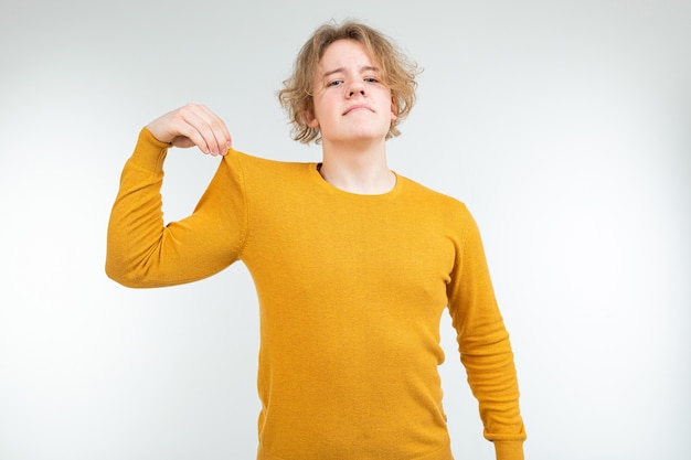 Handsome wavy blond young man in a yellow sweater is holding on to his cotton sweater on a white background.