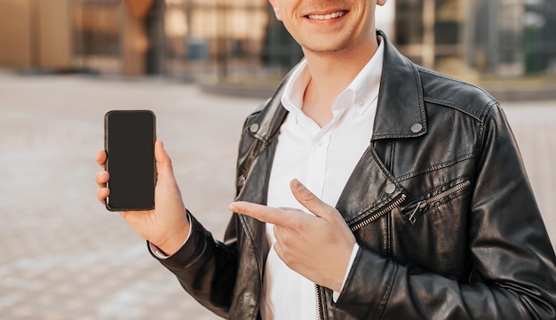 Handsome with a smartphone on the street of a big city Businessman points finger at phone screen on urban background