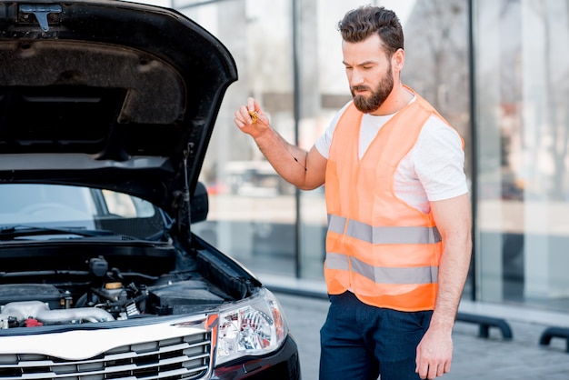 Handsome worker of an technical assistance service checking oil level in the car