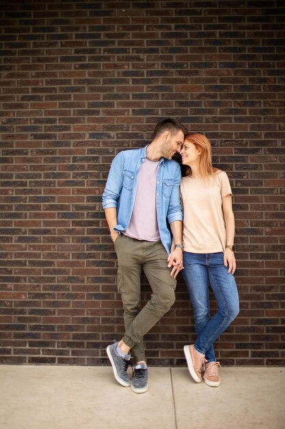 Handsome ymiling young couple in love in front of house brick wall