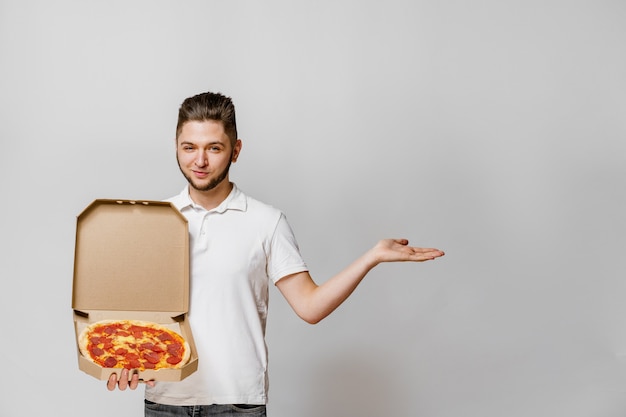 Handsome yound courier with pizza points to empty space for text advertise