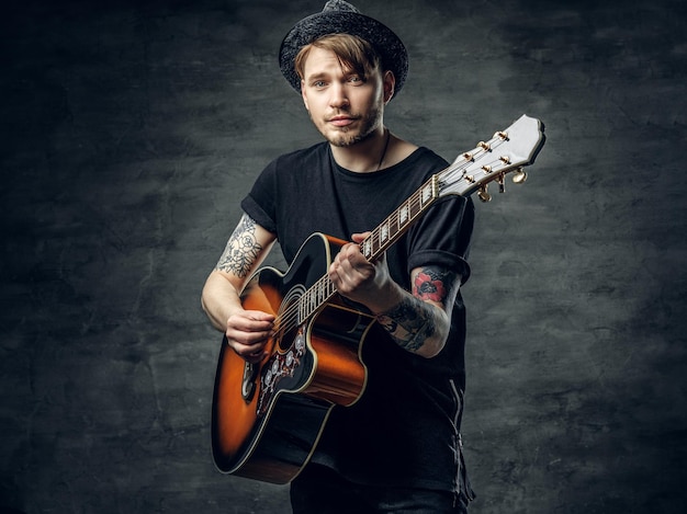 Handsome young acoustic guitar blues player with tattoos on arms performing his musical skills.