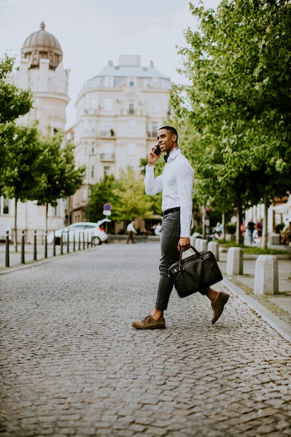 Handsome young African American businessman using a mobile phone while ceossing a street