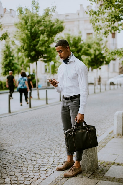 Bel giovane uomo d'affari afroamericano utilizzando un telefono cellulare mentre si aspetta un taxi in attesa di un taxi in strada