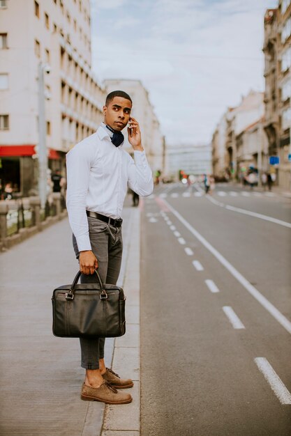 Handsome young African American businessman using a mobile phone while waitng for a taxi waitng a taxi in the street