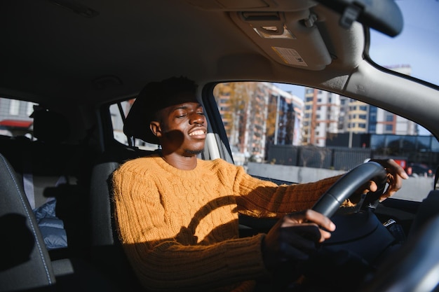 Handsome young African American man in his new high-tech electric vehicle while drinking. Self driving vehicle concept