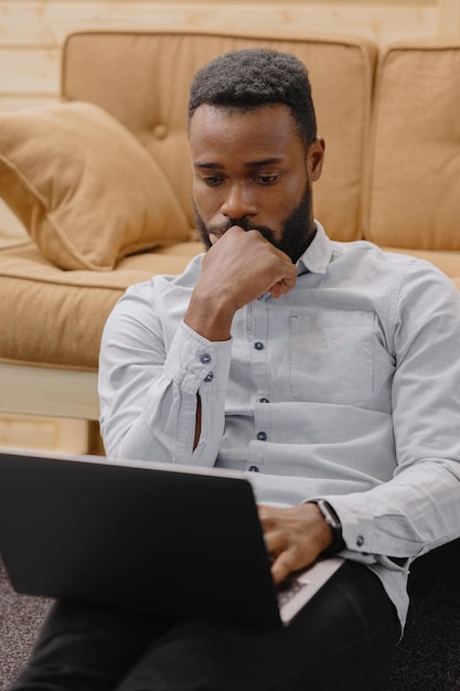 A handsome and young african american man in an office or coworking works on a laptop