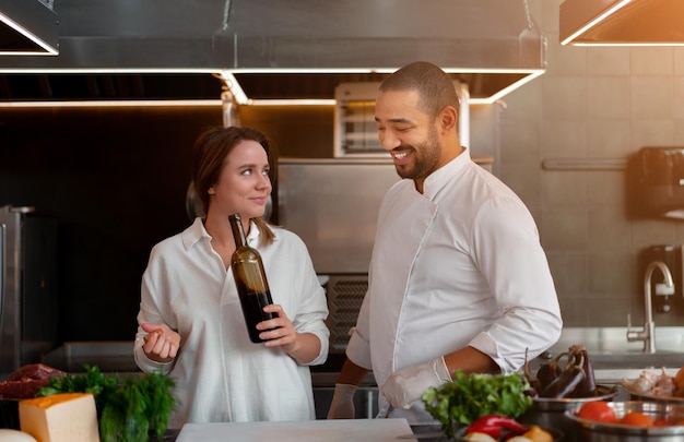 Handsome young African chef is cooking together with Caucasian girlfriend in the kitchen using red wine ingredient A cook teaches a girl how to cook Man and woman cooking in professional kitchen