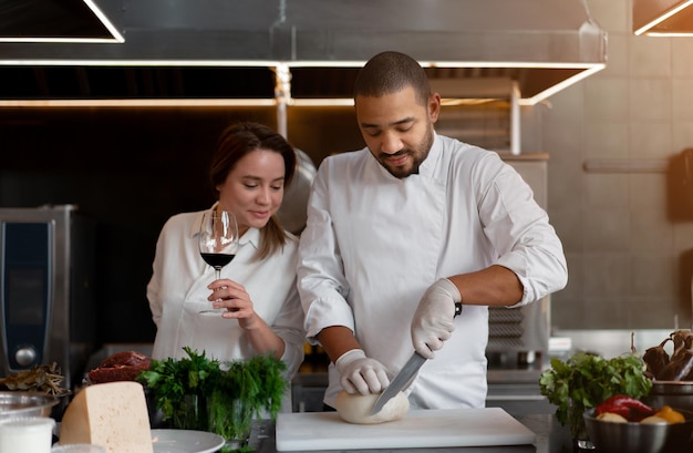 Il giovane chef africano bello sta cucinando insieme alla ragazza caucasica in cucina usando l'ingrediente del vino rosso un cuoco insegna a una ragazza come cucinare uomo e donna che cucinano in una cucina professionale