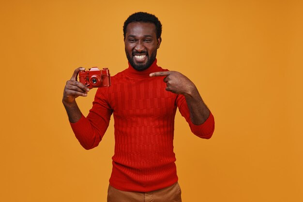 Handsome young African man in casual clothing smiling and pointing his camera