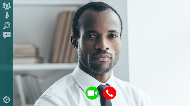 Photo handsome young african man in full suit looking at camera while having video call