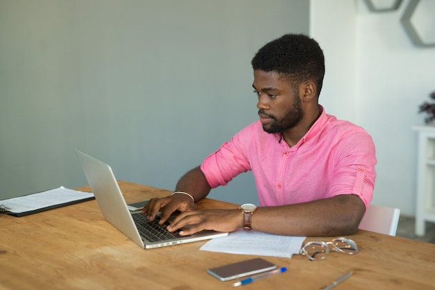 Bel giovane africano in ufficio a tavola con il computer portatile