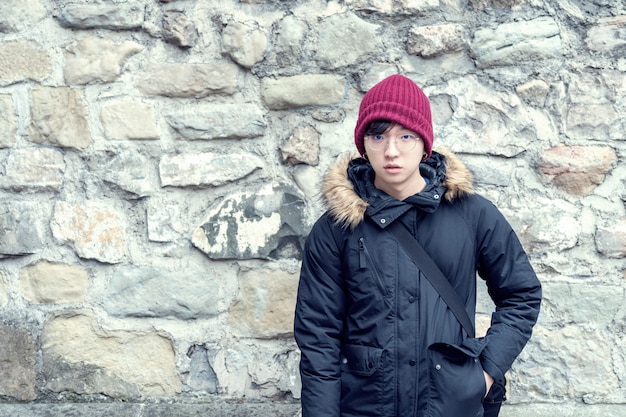 Handsome young asian guy in a Sweater Jacket near a old rock wall. 