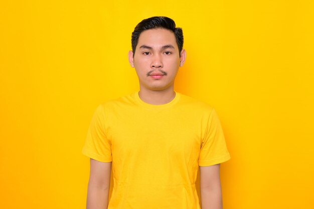 Handsome young Asian man in casual tshirt looking at camera with confident expression isolated on yellow background People lifestyle concept