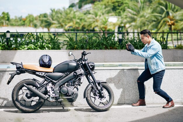 写真 スマートフォンで彼のバイクの写真を撮るハンサムな若いアジア人