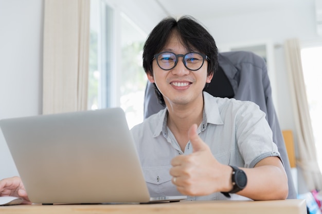 Handsome young Asian man thumbs up while sitting and working for business successfully