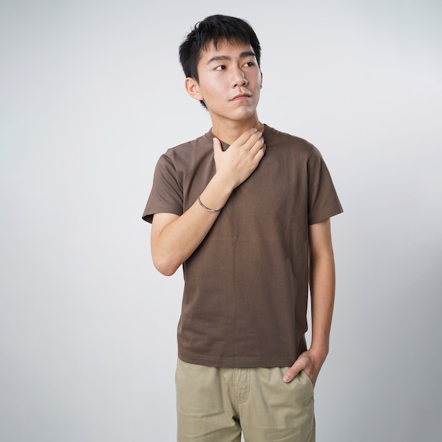 Handsome young asian man tshirt touching neck isolated gray wall