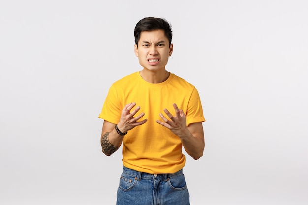 Handsome young asian man in yellow t-shirt clenching fists in rage