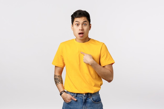 Красивый молодой азиатский человек в желтой футболке указывая к себе