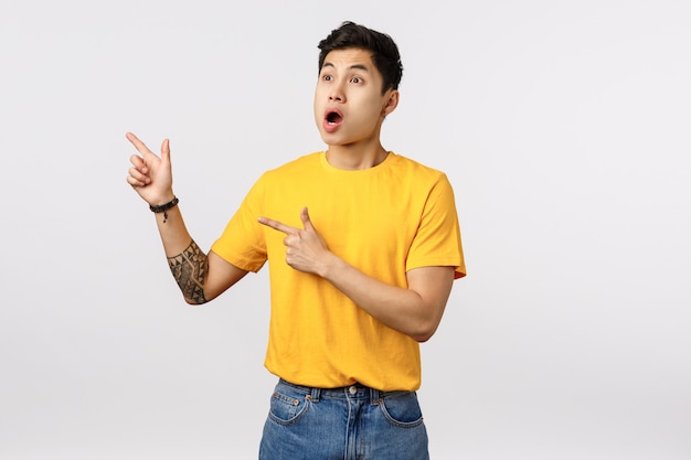 Handsome young asian man in yellow t-shirt pointing to the side