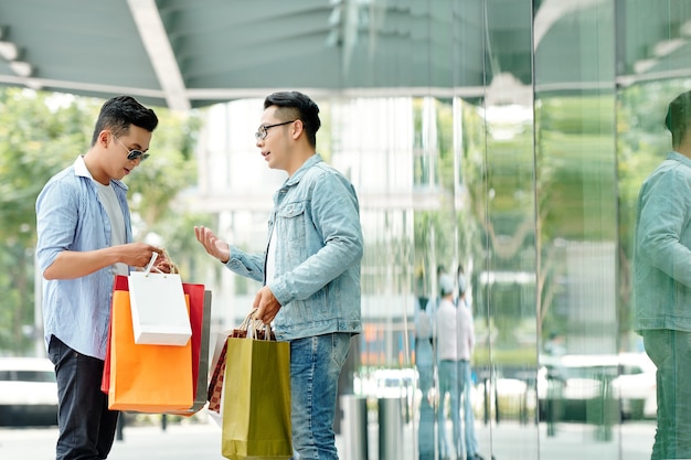 ショッピングバッグを持ったハンサムな若いアジア人男性がモールの外に立って購入について話し合っている