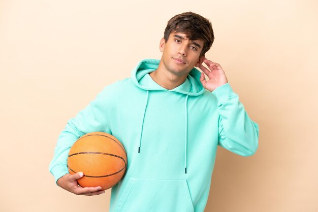 Handsome young basketball player man isolated on ocher background having doubts