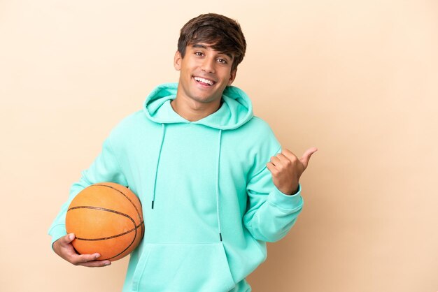 製品を提示する側を指している黄土色の背景に分離されたハンサムな若いバスケットボール選手の男