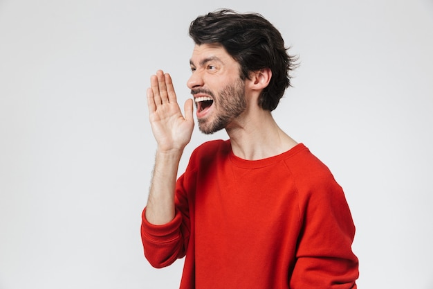 Handsome young bearded brunette man wearing sweater standing over white, screaming loud