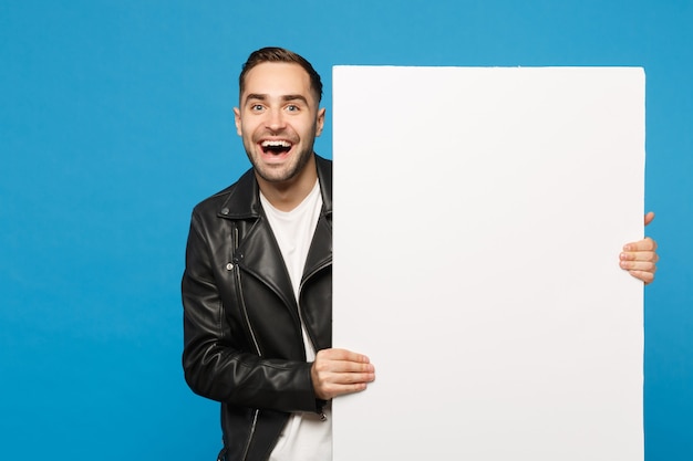 Bel giovane uomo barbuto tenere grande cartellone bianco vuoto vuoto per contenuti promozionali isolato su parete blu sfondo ritratto in studio. concetto di stile di vita di persone sincere emozioni. mock up copia spazio.