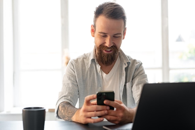 Handsome young bearded man spending time at home with phone in hands