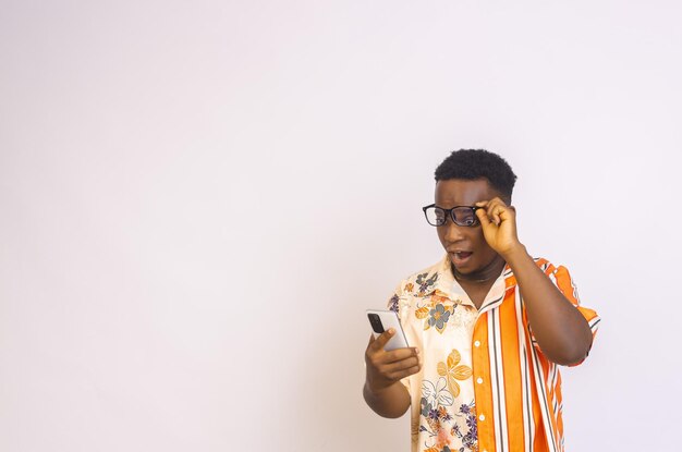 Handsome young black African male holding his glasses holding and looking into his phone surprised