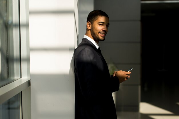 Красивый молодой черный человек с мобильным телефоном в офисе