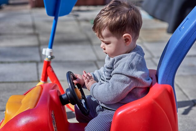 ハンサムな若い男の子の幼児が赤いプッシュカーで遊んでいる