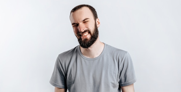 Handsome young brunette man frowning and closing eyes, angry on white background with space for advertising mock up