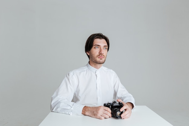 Handsome young brunette man sitting at the table holding front isolated on the gray wall