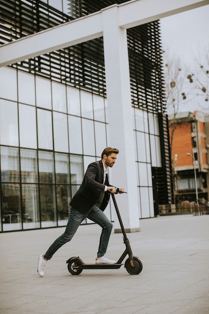 Handsome young business man in a casual clothes riding an electric scooter by an office building on a business meeting