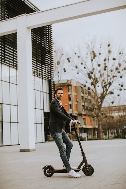 Handsome young business man in a casual clothes riding an electric scooter by an office building on a business meeting