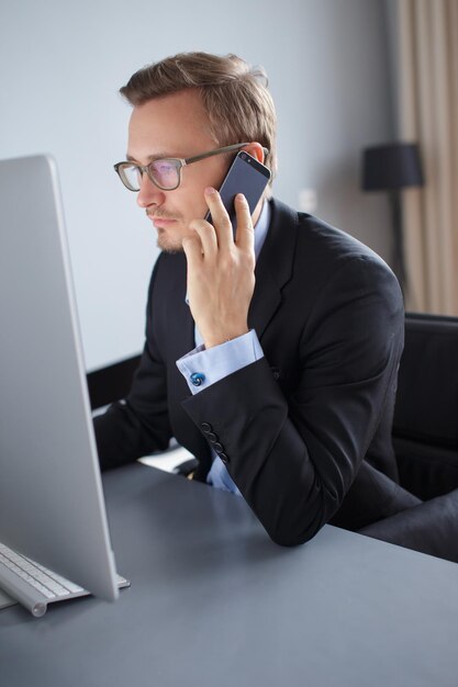 Photo handsome young business man colling with mobile phone and working with computer in office.