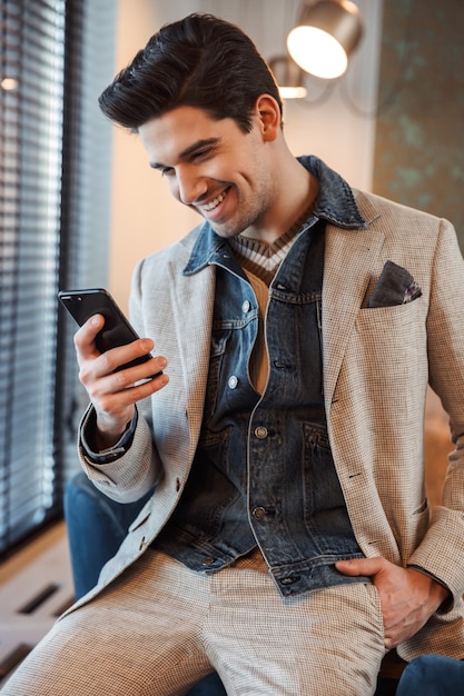 handsome young business man posing indoors in office using mobile phone.