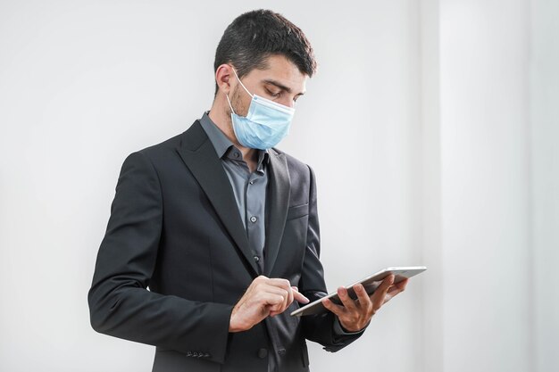 Handsome young business man wearing protective mask working with tablet in a white background