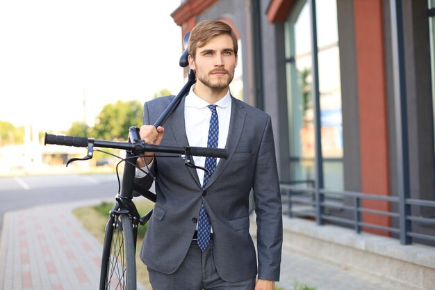 Bel giovane uomo d'affari che porta la sua bicicletta sulla spalla mentre si cammina all'aperto.