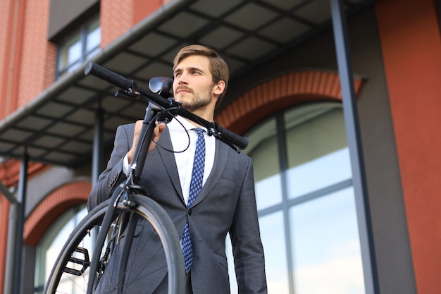 屋外を歩きながら彼の肩に自転車を運ぶハンサムな青年実業家。