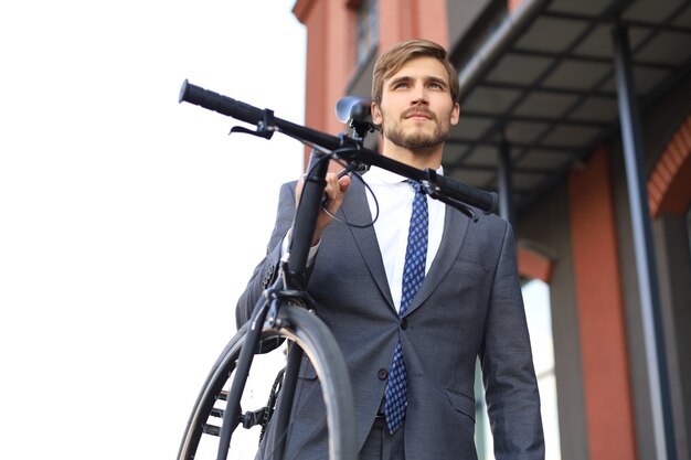 Handsome young businessman carrying his bicycle on shoulder while walking outdoors.