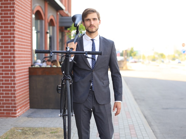 Handsome young businessman carrying his bicycle on shoulder while walking outdoors.